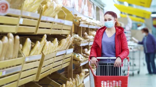 Alışveriş arabalı bir kadın salgın sırasında ekmek raflarının yanında poz veriyor. — Stok video