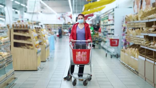 Frau mit Einkaufswagen während Pandemie im Supermarkt zwischen Gängen — Stockvideo