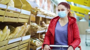 Maskeli genç kadın süpermarkette ekmek raflarının yanında poz veriyor.
