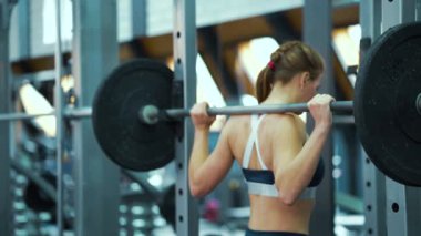 Spor salonunda halterle çömelmiş bir kadın.