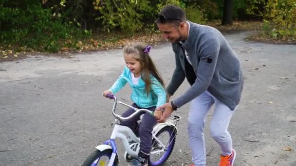 Vader die dochter rijles geeft op de fiets in park — Stockvideo