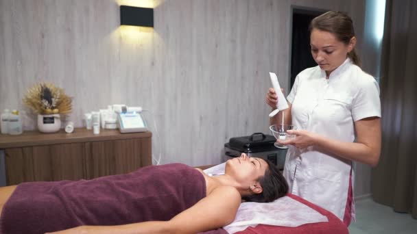 Kosmetyczka stosująca krem przeciwzmarszczkowy na twarz klientki w spa wellness — Wideo stockowe