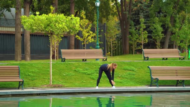 Passform kvinna värmer upp nära damm i parken — Stockvideo