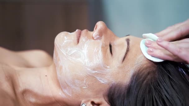 Hände der Kosmetikerin entfernen Creme aus dem Gesicht der Frau — Stockvideo