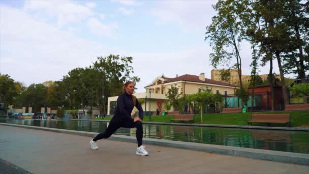 Fit kobieta rozciągająca nogi w pobliżu stawu w parku — Wideo stockowe
