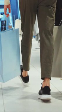 Alışveriş merkezinde elinde kağıt torbalarla dolaşan, tüketim, perakende ve modern yaşam tarzını sembolize eden kişiye yakından bakın.