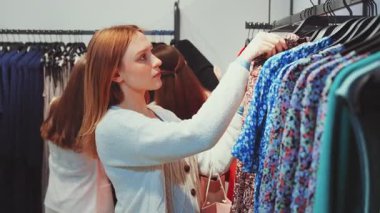 Moda mağazasında alışveriş yapan genç bir kadın, raflarda renkli elbiseler gezen, modern yaşam tarzını, perakende kıyafetlerini ve stil seçimini seven bir kadın.