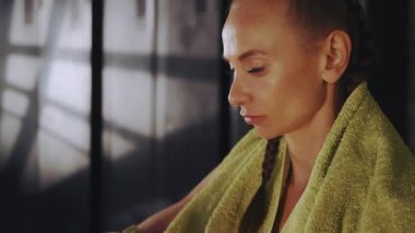 Odaklanmış, saçları örgülü, spor salonunda boks antrenmanından önce pembe el ambalajı takan omuzlarında havluyla zihinsel olarak zorlu bir antrenman için hazırlanan bir kadın.