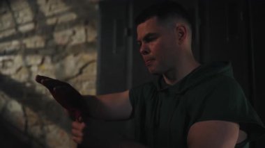 Koyu renk spor salonundaki kararlı adam kırmızı el ambalajlarını ayarlar, tuğla duvara karşı durur, zihinsel olarak yoğun eğitime hazırlanır. Kavram: Güç, dayanıklılık