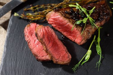 az pişmiş biftek kara angus üstten görünüm bezelye filiz kekik biberiye baharat ile siyah dikdörtgen plaka üzerinde dilimlenmiş