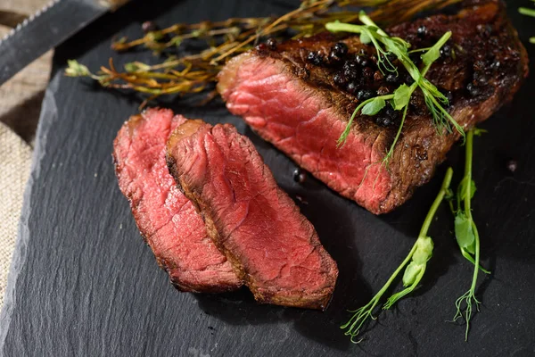 az pişmiş biftek kara angus üstten görünüm bezelye filiz kekik biberiye baharat ile siyah dikdörtgen plaka üzerinde dilimlenmiş