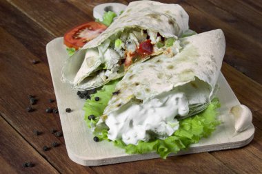 Shaurma, kesilmiş yarısında, bir eski ahşap rustik arka plan üzerinde domates ve biber ile ahşap bir gemide bir ekmek pasta sebzeli et