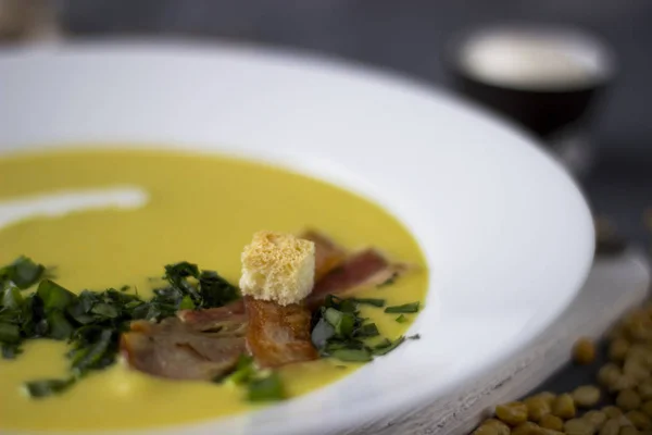 Zuppa di piselli con pezzi di pancetta, prezzemolo e cipolla in una ciotola su un — Foto Stock