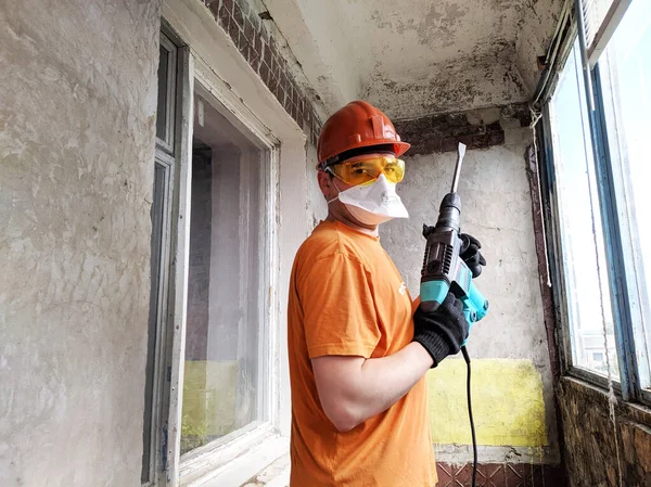 A man with a hammer drill in his hands. Worker with hammer breaking interior wall plastering