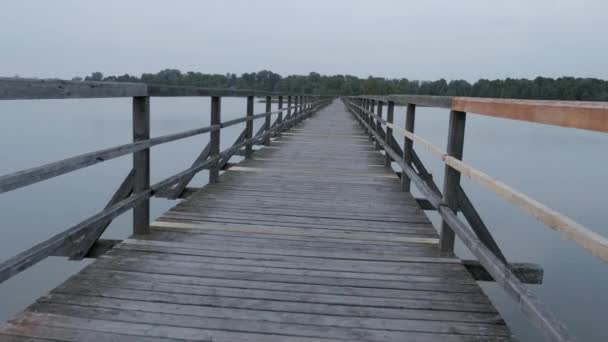 Eine Person, die allein an einem alten Holzsteg oder einer Brücke über den Fluss spaziert. Ruhe und Entspannung — Stockvideo