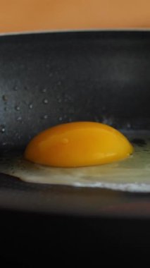 Yapışmayan tavada taze yumurta cızırtısı, yakın çekim pişirme çekimi. Dikey video.