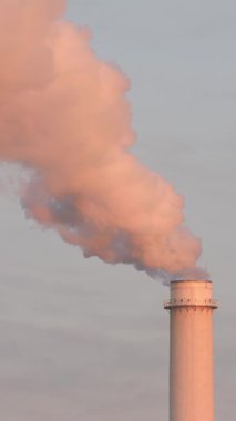 Bir bacadan yayılan duman, batan güneş tarafından boyanmış. Dikey video.