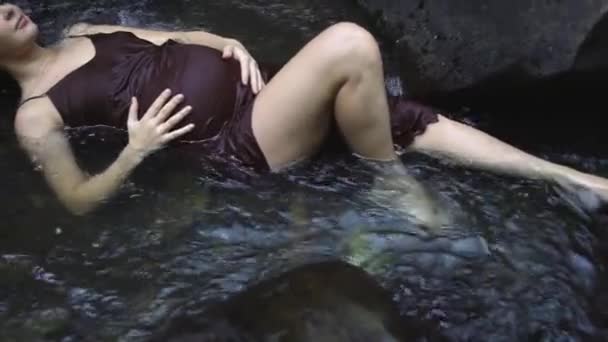 Zwaar zwangere vrouw liggend in de rivier genieten van de harmonie met de natuur en wachten op de baby. Slow Motion. — Stockvideo