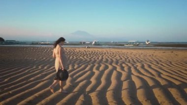 Esmer hamile neşeli kadın gün batımında kumlu bir plajda tek başına yürüyüş