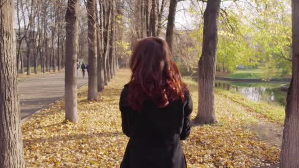 Eine glückliche junge Frau wirft im Herbstpark umgefallenes Laub in die Kamera. Zeitlupe — Stockvideo