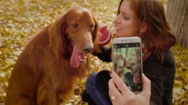 Neşeli kız sonbahar parkta köpek ayarlayıcı ile akıllı telefonda selfie yapar