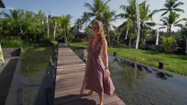 Jeune femme élancée dans une longue robe marchant dans un hôtel de villégiature. Vue de derrière, Stadicam shot. 4K — Video