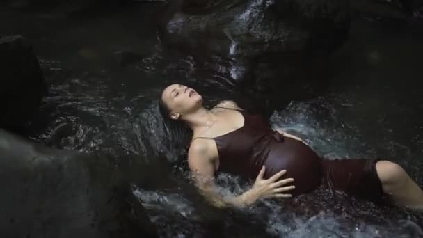 Hermosa mujer embarazada en un vestido de color marrón oscuro se encuentra y se relaja en el agua del río. Movimiento lento . — Vídeos de Stock