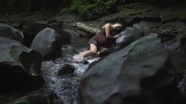 Atractiva mujer embarazada con un vestido marrón oscuro miente y siente dolor contracciones de parto en la selva tropical rive. Movimiento lento . — Vídeo de stock