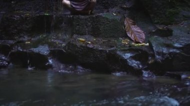 Duş sonra tropikal orman Nehri kıyısında oturan koyu kahverengi bir elbise mutlu hamile kadın. Yavaş hareket.