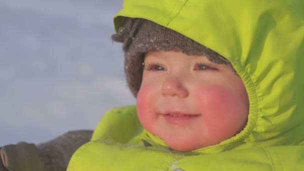 Gros plan du visage bébé souriant aux joues roses hiver en plein air par temps enneigé et ensoleillé — Video