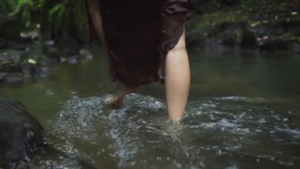 Schöne schwangere Frau in einem dunkelbraunen Kleid geht barfuß auf dem Wasser im tropischen Dschungel Fluss. Zeitlupe. — Stockvideo