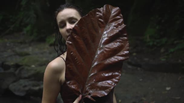 Retrato de una hermosa mujer embarazada con una enorme hoja de árbol en sus manos junto a un río tropical en la selva. Movimiento lento . — Vídeo de stock