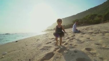 Küçük sarışın kız güneşli bir günde babasının yanında kumlu bir plajda yürüyor