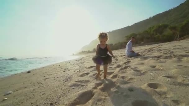 Klein blond meisje loopt op een zandstrand naast haar vader op zonnige dag — Stockvideo