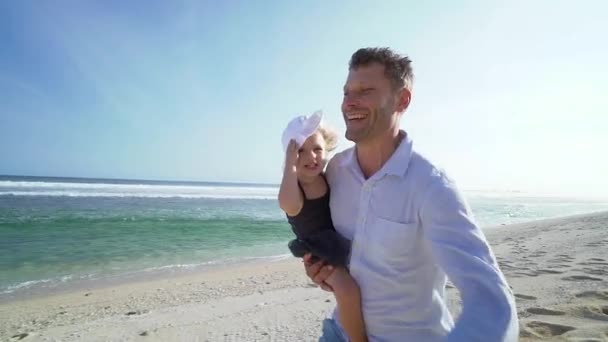 幸せな笑顔の父は手にかわいい娘を保持し、晴れた日にビーチで実行しています — ストック動画