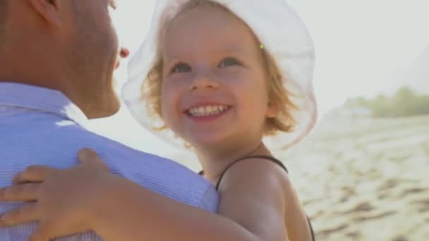 Close up tiro de sorrir pequena filha abraçando o pai em seus braços à beira-mar . — Vídeo de Stock