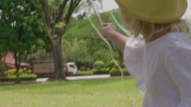 Liten flicka i vit klänning och hatt blåser stora tvål bubblor i parken. Slow motion — Stockvideo