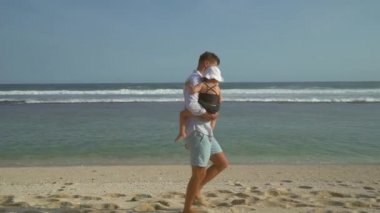 Mutlu baba elinde sevimli kızı tutar ve güneşli bir günde sahilde yürüyüş