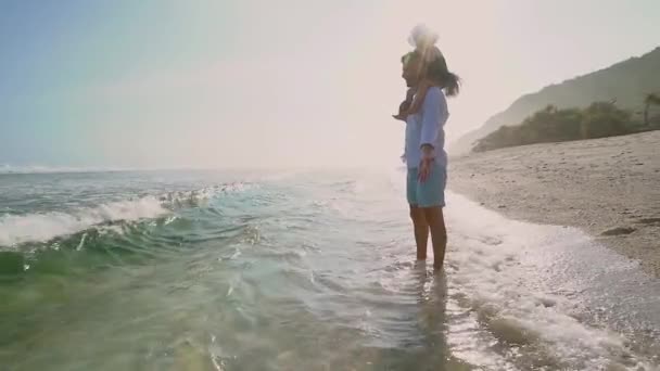 Μικρό κορίτσι κάθεται σε μπαμπάδες ώμους στην παραλία σε μια ηλιόλουστη μέρα — Αρχείο Βίντεο