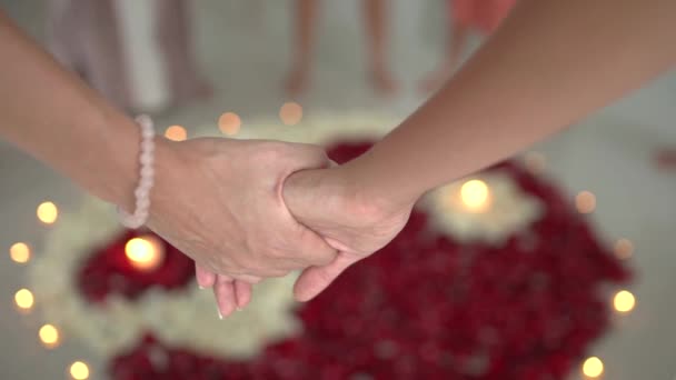 Primer plano de dos mujeres uniendo las manos en el fondo un mandala pétalo de rosa con velas durante la práctica espiritual — Vídeos de Stock