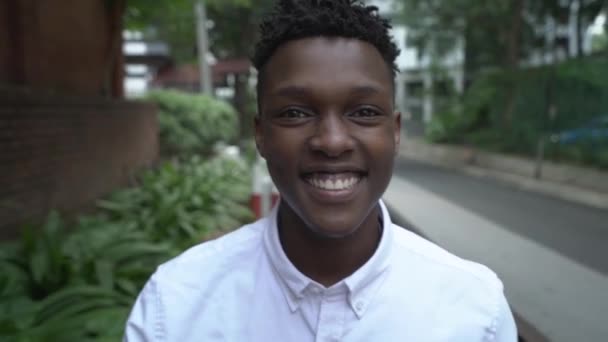 Gros plan d'un beau jeune Africain souriant marchant dans la rue et regardant la caméra . — Video