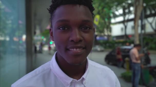 Крупный план улыбающегося красивого африканского молодого человека на улице в неоновом свете и смотрящего в камеру . — стоковое видео