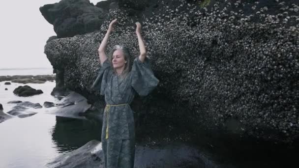 Ung kvinna med strand av naturligt grått hår på bakgrunden av en sten täckt med skal vid havet — Stockvideo