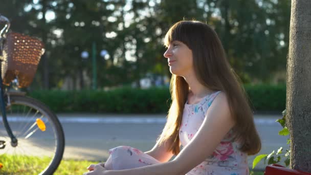 Giovane donna innamorata seduta da sola nel parco, sorridendo a se stessa, sognando ad occhi aperti — Video Stock