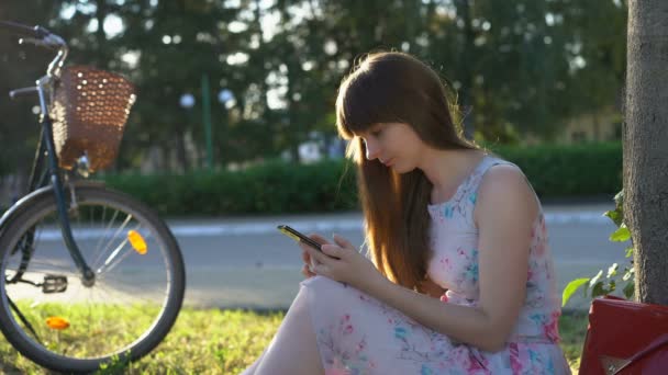 Mooie vrouw zittend in Park, scrollen feed op haar Smartphone, genieten van de zomer — Stockvideo