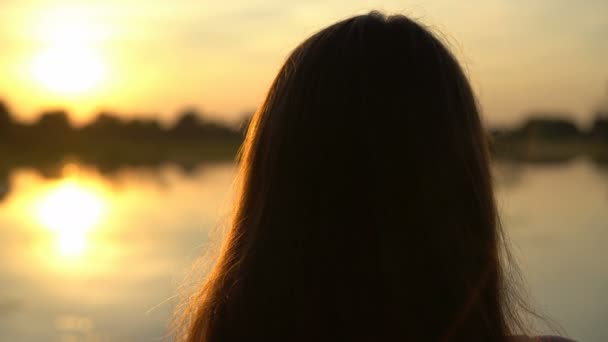 Jonge vrouw kijkt naar zonsondergang in de buurt van het meer, genieten van de zomer, eenzaamheid — Stockvideo