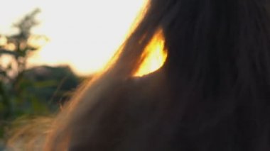 Gün batımında yavaş çekimde dans eden, gülümseyen, saçlarını sallayan çekici genç bir kadın.