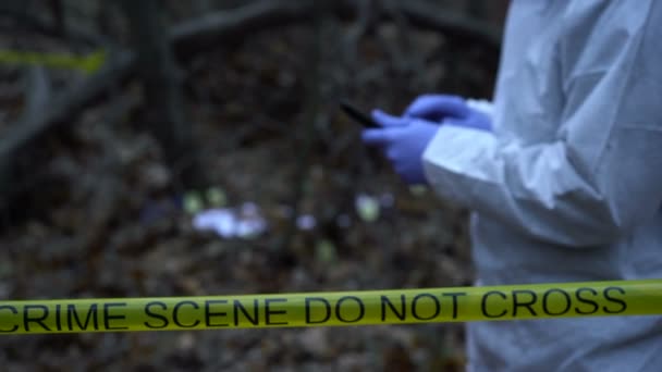 Сотрудник криминалистической лаборатории вводит данные на планшете на месте преступления в лесу — стоковое видео