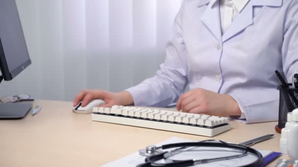 Врач за компьютером в офисе, врач проверяет медицинские записи — стоковое видео