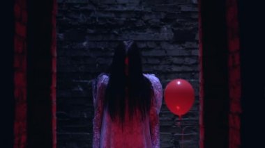 Beyaz elbiseli kız elinde kırmızı balonla karanlıkta kurbanını bekliyor.